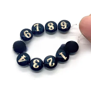 Dettaglio di perle tonde nere da 8mm con numeri arabi dorati per la creazione di gioielli