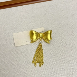 Vintage gold bow tassel brooch with pearl accent on minimalist textured fabric background