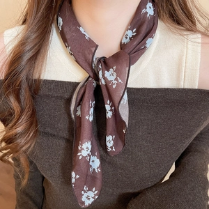 Close-up of a brown silk scarf with blue floral print tied in a stylish neck knot