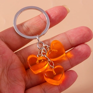 Detail of three orange jelly heart pendants on a silver metal keychain held by hand