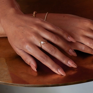 Detail of 18K gold stainless steel wavy ring with oval white zircon on a model hand