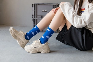 Detailed close-up of blue cotton mid-calf socks with white cloud pattern and beige sneakers