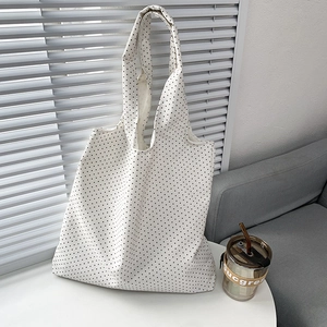Detailed close-up of a white canvas tote bag with black polka dots on a white table