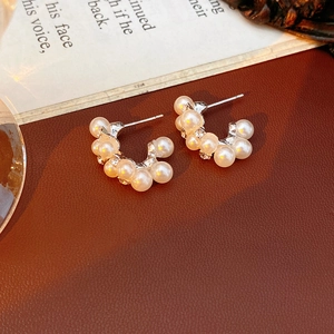 Detalle macro de pendientes de perlas en forma de C con baño de plata y pedrería