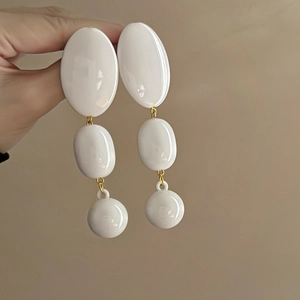 Chic white acrylic oval drop earrings with gold metal links shown in hand