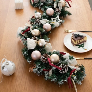 Deluxe Christmas garland with pine cones, pink ornaments and bows on wooden table