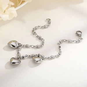 Detailed close-up of a silver heart charm bracelet on a textured beige background