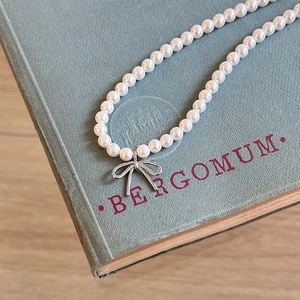 Elegant pearl necklace with silver bow pendant displayed on a vintage light blue book cover