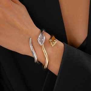 Close-up of sleek gold and silver snake-shaped open bracelets on a model's wrist