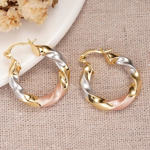 Detail of tricolor twist hoop earrings in gold silver and rose gold on beige fabric