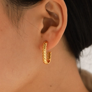 Close-up of gold C-shaped twisted earrings featuring woven texture on a model's ear