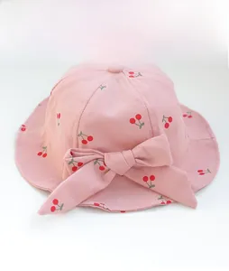 Pink cotton baby sun hat with red cherry patterns and a large decorative bow on front