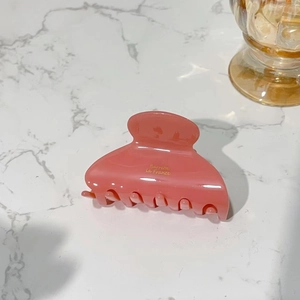 Detailed top view of a pink acetate claw clip with gold lettering on marble background