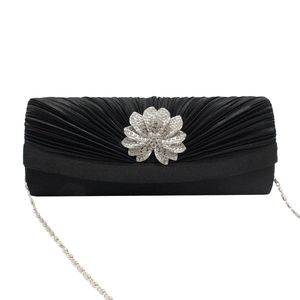 Macro detail of black pleated satin evening clutch with silver rhinestone flower and chain