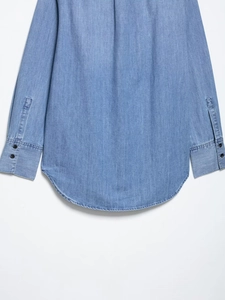 Detail of light blue denim shirt showing curved hem and double-button cuffs on white background
