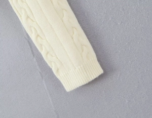 Gros plan du poignet d'un pull blanc cassé montrant les mailles torsadées et côtelées