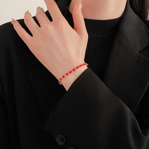 Detail of red beaded gold chain bracelet on model wrist with black suit background