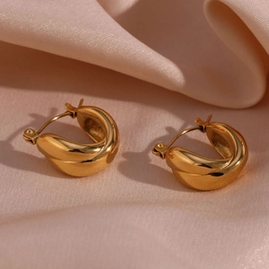 Macro shot of gold twisted hoop earrings resting on elegant pink silk fabric background
