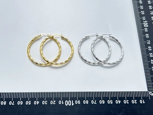 Detailed view of large twisted rope hoop earrings in gold and silver with ruler scale