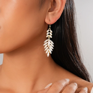 Detail of elegant gold leaf-shaped earrings with white crystals on female model