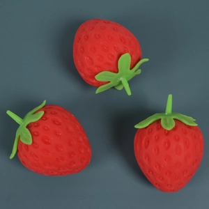 Three realistic red strawberry squishy toys on a dark grey background from a top-down view