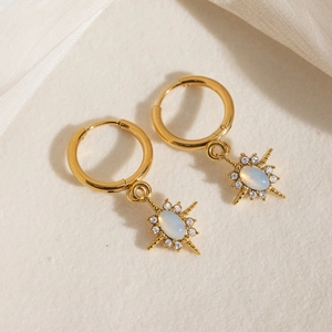 Elegant gold starburst drop earrings with opal stone and white rhinestones on white fabric