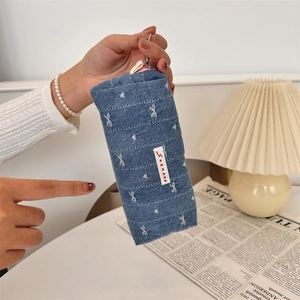 Hand holding a blue denim pencil case with white embroidery and silver zipper detail