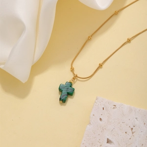 Detailed close-up of a golden cross necklace with green natural stone and beaded chain