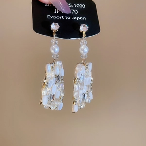 Macro detail of geometric pendant earrings with pearls, crystals, and gold frames