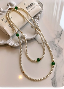 Detail of elegant double-layer white pearl necklace with green accent beads on ceramic tray