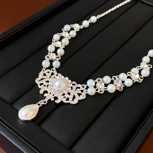 Vue macro d'un collier de perles baroques avec motif floral serti de diamants et goutte