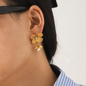 Close-up of gold flower earrings with pearl detail worn by a model in soft lighting