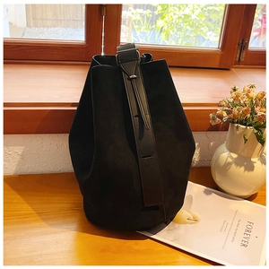 Minimalist black suede bucket bag on a wooden windowsill with natural sunlight and dried flowers