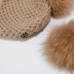 Detail of camel knit beanie featuring thick texture and detachable fluffy fur pom-pom