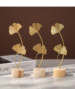 Three golden ginkgo leaf ornaments with round wooden bases on a dark table setup
