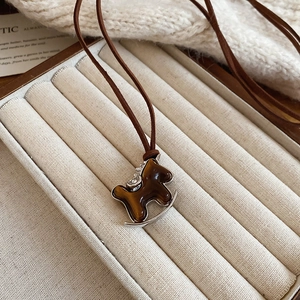 Macro detail of a vintage-style rocking horse pendant necklace on a cream velvet gift box