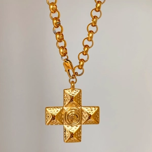 Macro detail of 18k gold plated cross pendant with embossed relief texture and rolo chain