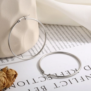 Detailed view of large silver stainless steel hoop earrings on a minimalist background