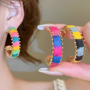 Detailed macro view of handmade colorful thread-wrapped C-shape earrings with gold bead trim