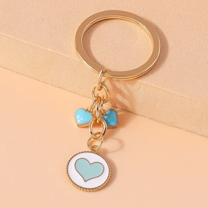 Detail of golden metal keychain with blue and white enamel heart charms on peach background