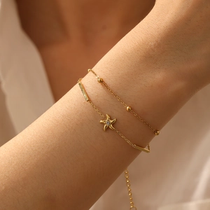 Detail of a layered gold-plated bracelet with starfish charms on a female wrist