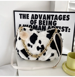 Detailed shot of cow print plush tote bag with gold chain and furry ball charm