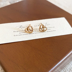 Close-up of golden heart knot earrings featuring an intricate hollow interwoven design