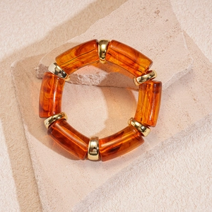 Close-up of amber acrylic elastic bracelet with golden metal spacers on stone surface