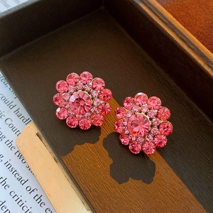 Macro shot of pink crystal flower earrings on a vintage wooden tray and antique paper