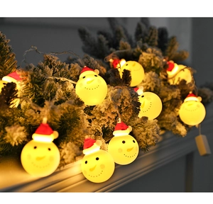 Close-up of LED snowman fairy lights with warm yellow glow on snow-covered pine branches