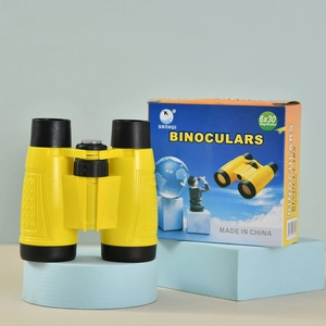 Macro shot of yellow 6x30 binoculars for kids with colorful packaging on blue stand