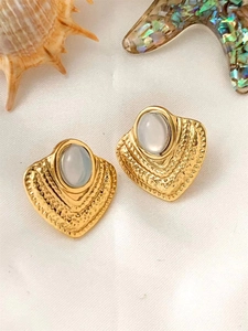 Close-up of golden heart earrings with opal stones on white satin with seashells