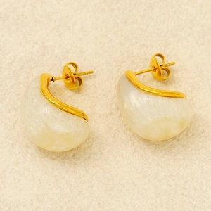 Detail of drop-shaped gold earrings with white pearlescent resin on beige texture