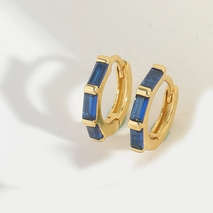 Macro detail of gold hoop earrings featuring four horizontal blue baguette cut stones